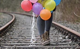 Girl walking down train tracks holding balloons