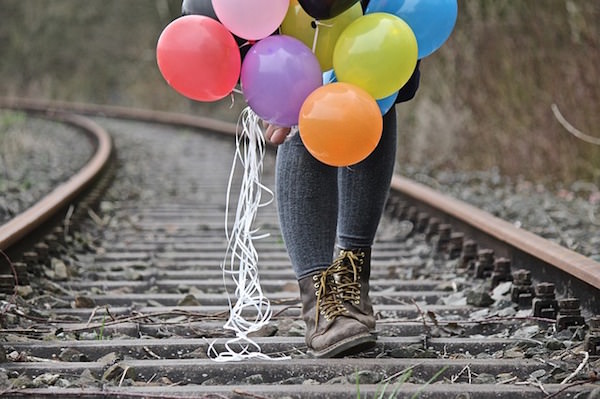 Girl walking down train tracks holding balloons