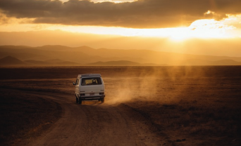 Van drives down dusty road at sunset