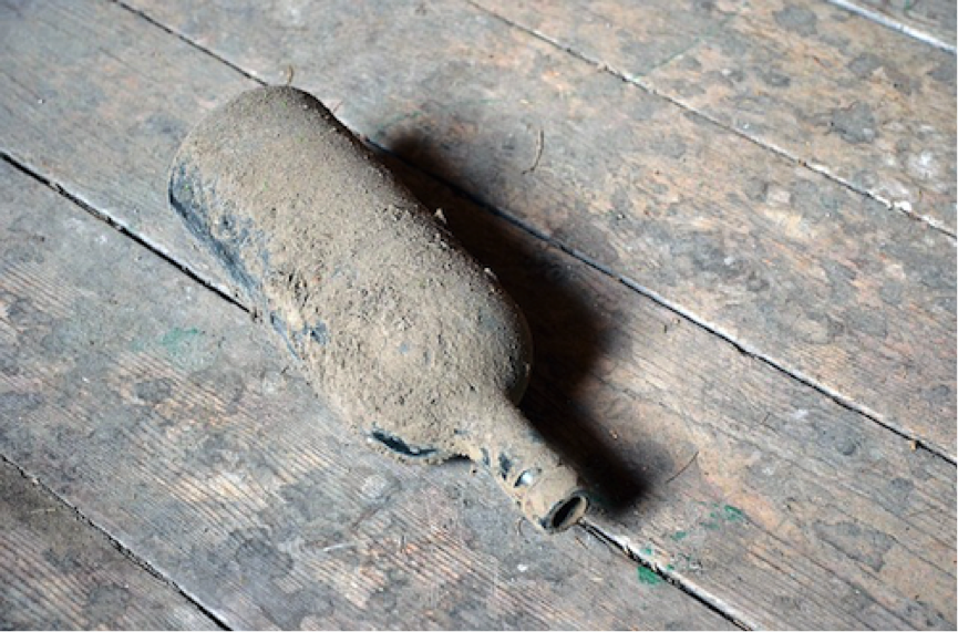glass bottle covered in dust on floorboards